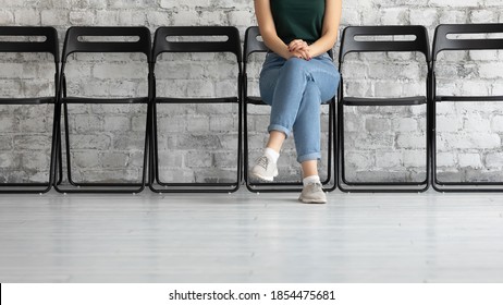 Waiting time. Cropped view of young female job applicant or public officer visitor sitting cross legged on chair in corridor close to hr or functionary office showing confidence patience, copy space