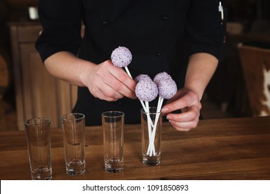 Waitress arranging candy bar. Putting cake pops with pink icing into glasses, closeup. Dessert table and catering concept for party, birthday, wedding and other holiday celebration - Powered by Shutterstock