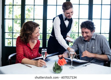 Waitress assisting a couple while selecting menu from menu card