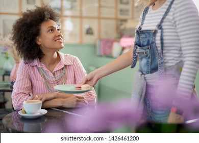 Waitress bringing cookies to a beautiful mixed race woman. Pastry shop interior. - Powered by Shutterstock