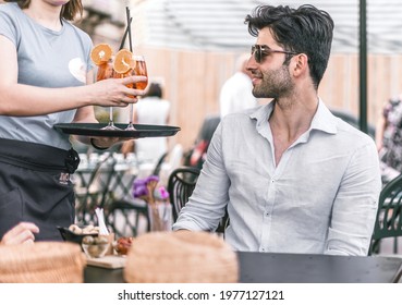 A waitress brings a tray of cocktails to a young man's table. Alcohol lifestyle concept. - Powered by Shutterstock