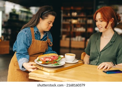 Waitress with Down syndrome serving a customer a sandwich and coffee in a trendy cafe. Professional woman with an intellectual disability working in a fast food restaurant.
