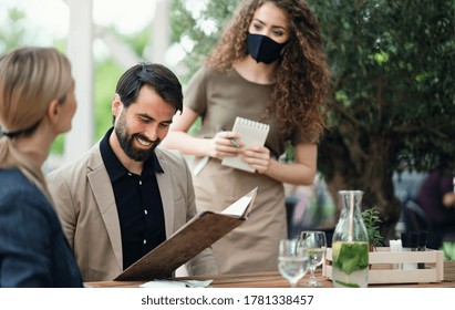 Waitress with face mask serving happy couple outdoors on terrace restaurant. - Powered by Shutterstock