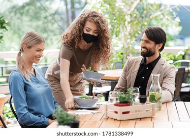 Waitress With Face Mask Serving Happy Couple Outdoors On Terrace Restaurant.