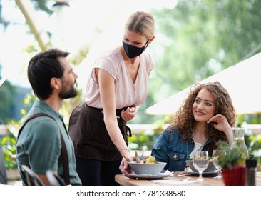 Waitress with face mask serving happy couple outdoors on terrace restaurant. - Powered by Shutterstock