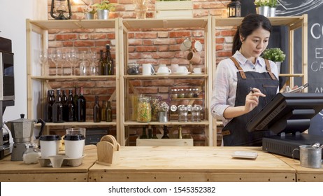 waitress girl in apron using finger touching screen of POS terminal in coffee shop. young woman staff in coffeehouse checking on tablet with software interface to take order and print receipt in cafe - Powered by Shutterstock