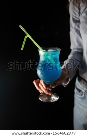 waitress holding blue lagoon cocktail on black background with copy space. night club and bar concept