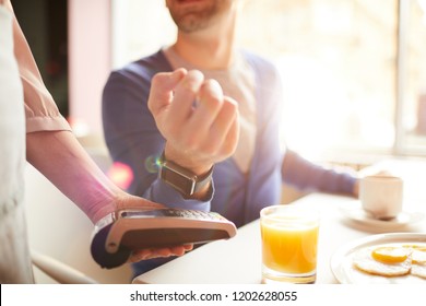 Waitress holding electronic payment machine while client paying for order by smartwatch on his wrist - Powered by Shutterstock