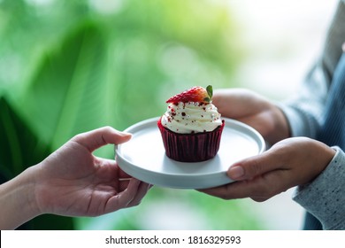 A waitress holding and serving a piece of red velvet cupcake to customer - Powered by Shutterstock