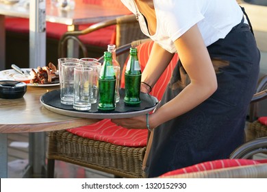 A Waitress Is Holding A Tray With Dirty Dishes And Leftover Food. Waitress Cleaning The Table In A Restaurant. The Concept Of Service.