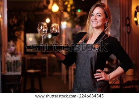 Waitress looking at the camera and smiling while posing holding a tray with wine glasses.