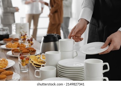 Waitress near table with dishware and different delicious snacks during coffee break, closeup - Shutterstock ID 2149827341