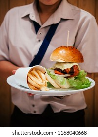 Waitress Serving Fresh Tasty Large Cheese BLT Burger With French Fries On White Plate