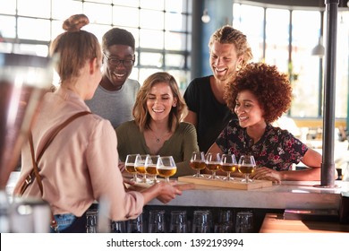 Waitress Serving Group Of Friends Beer Tasting In Bar