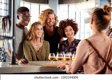 Waitress Serving Group Of Friends Beer Tasting In Bar