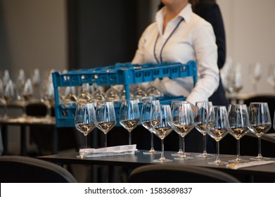 Waitress set the tables with crystal gobles for a wine tasting workshop. Catering service and dining room staff at work.
