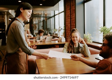 Waitress smiling while handing menu to seated customers in modern cozy cafe with large windows featuring natural light. Patrons and staff interacting in welcoming atmosphere - Powered by Shutterstock