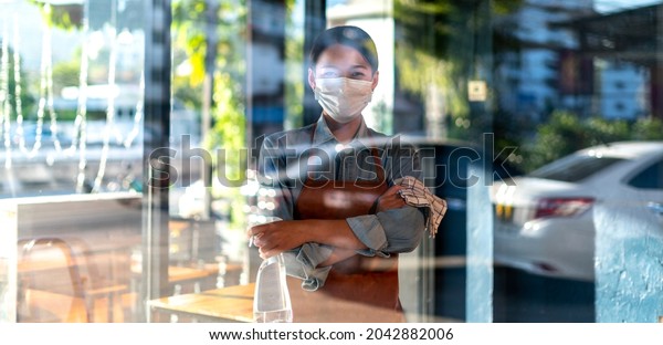Waitress\
Staff with face mask using alcohol spray to clean Cafe, Restaurant,\
or Hotel Bar. Hygiene, safety  Antiseptic, cleanliness, healthcare,\
anti-virus, Anti Coronavirus (COVID-19)\
Concept.