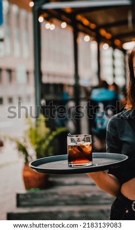 waitress standing in outdoor cafe. girl the waiter holds a tray with a glass of alcoholic cocktail