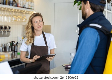 Waitress with tablet serving customer at cafe counter in modern interior