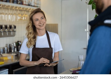 Waitress with tablet serving customer at cafe counter in modern interior