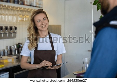 Waitress with tablet serving customer at cafe counter in modern interior