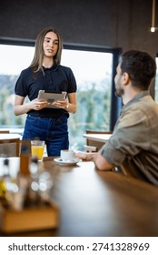 Waitress using a digital tablet to take a food order from a male guest in a cafe.