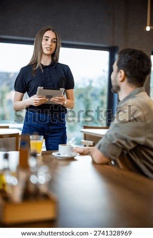 Waitress using a digital tablet to take a food order from a male guest in a cafe.