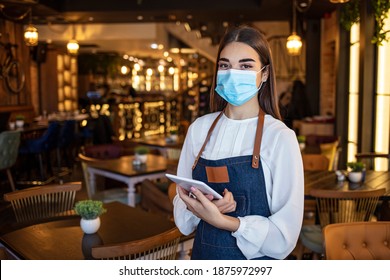 Waitress Working On Touchpad While Wearing Protective Face Mask. Beautiful Waitress Working At A Restaurant Wearing A Facemask. Waitress Wearing A Facemask And Using A Tablet Computer