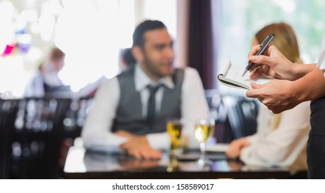 Waitress writing an order in front of two business people talking