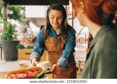 Waitron with Down syndrome serving a customer a sandwich and coffee in a trendy cafe. Professional woman with an intellectual disability working in a fast food restaurant.