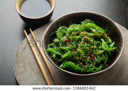 Wakame seaweed salad with sesame seeds and chili pepper in a bowl on a wooden slice 