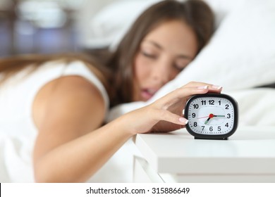 Wake up of an asleep girl stopping alarm clock on the bed in the morning