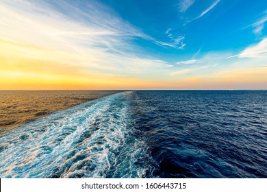 Wake from a boat in the deep blue sea during a warm, vibrant sunset
