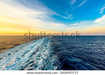 Wake from a boat in the deep blue sea during a warm, vibrant sunset