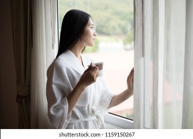 wake up :Woman in the morning holding a cup of tea or coffee and looking at the sunrise standing near the window in her home