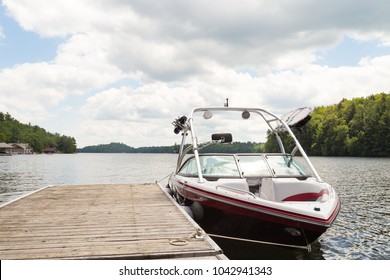 A wakeboard boat at a wooden dock in the Muskokas on a sunny day. 