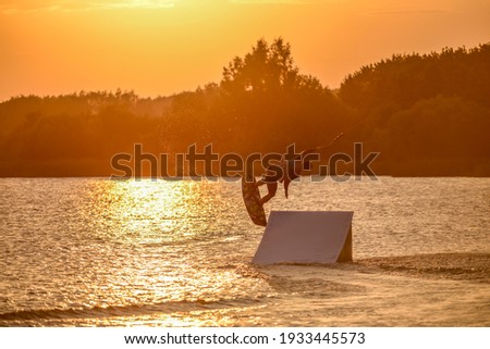 Wakeboarder making tricks. Low angle shot of man wakeboarding on a lake. Man water skiing at sunset.