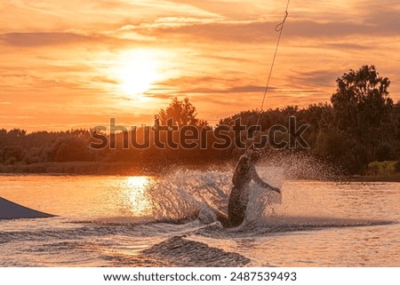 Wakeboarder making tricks. Low angle shot of man wakeboarding on a lake. Man water skiing at sunset.