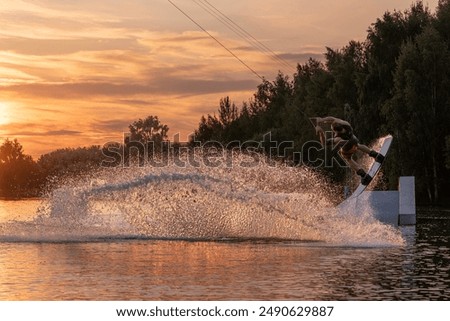 Wakeboarder making tricks. Low angle shot of man wakeboarding on a lake. Man water skiing at sunset.