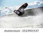  Wakeboarder making tricks while wakeboarding on lake. Young man surfer having fun wakesurfing in the cable park. Water sport, outdoor activity concept.