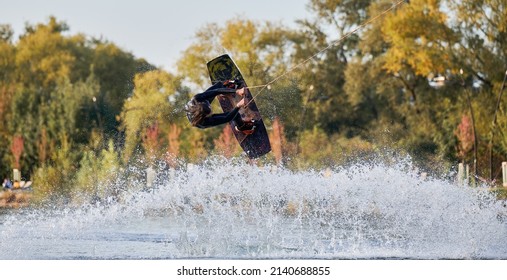 Wakeboarder making tricks while wakeboarding on lake. Young man surfer having fun wakesurfing in the cable park. Water sport, outdoor activity concept.