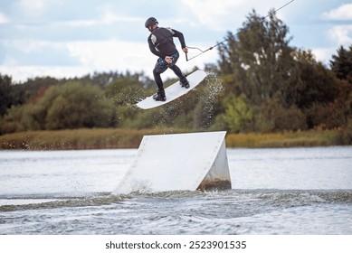  Wakeboarder making tricks while wakeboarding on lake. Young man surfer having fun wakesurfing in the cable park. Water sport, outdoor activity concept.