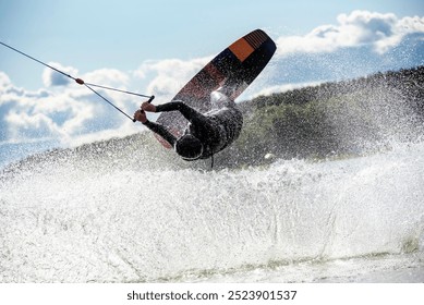  Wakeboarder making tricks while wakeboarding on lake. Young man surfer having fun wakesurfing in the cable park. Water sport, outdoor activity concept. - Powered by Shutterstock