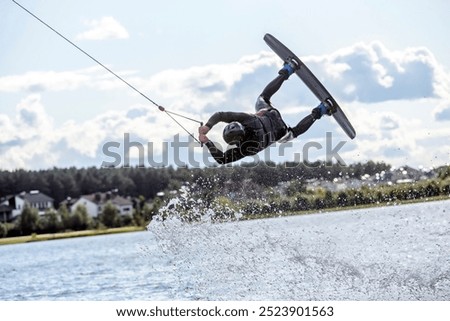  Wakeboarder making tricks while wakeboarding on lake. Young man surfer having fun wakesurfing in the cable park. Water sport, outdoor activity concept.