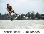 Wakeboarder surfing across a lake. A man wakeboards behind a boat.