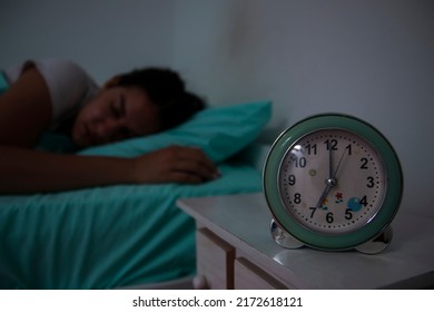 Waking Up Of An Asleep Girl Stopping Alarm Clock On The Bed In The Morning. Teen Girl Hates Waking Up Early In The Morning. Closeup Of Alarm Clock And Sleepy Teenager.