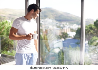 Waking up with fresh coffee and a great view. Cropped shot of a handsome young man drinking coffee while standing at his bedroom window. - Powered by Shutterstock