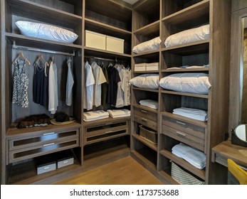 Walk In Closet With Wooden Shelves There Are Pillows And Hanging Clothes.