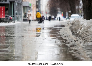 Walk on wet melted ice pavement. Back view on the feet of a man walking along the icy pavement. Pair of shoe on icy road in winter. Abstract empty blank winter weather background